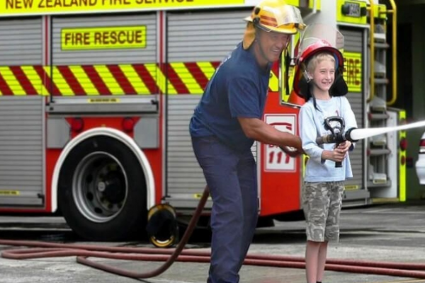 Older fireman lets a boy use the fire hose