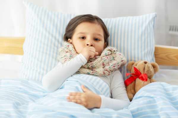 Girl coughing in bed with scarf and teddy bear