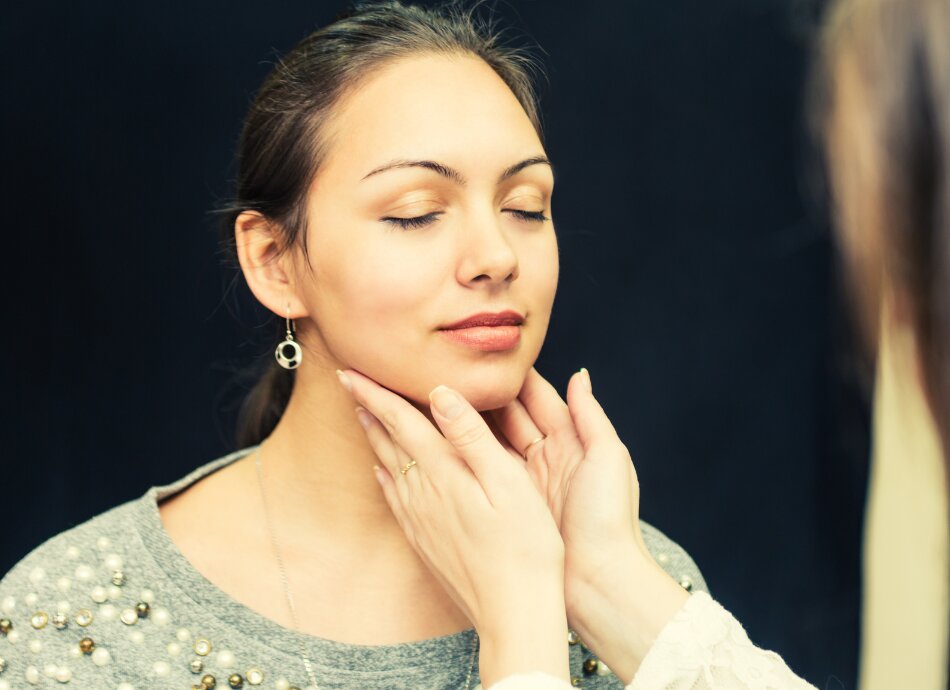 Hands feel for thyroid on young woman's throat