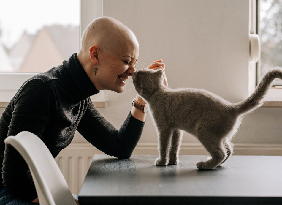 Bald young woman with cancer strokes cat on the table