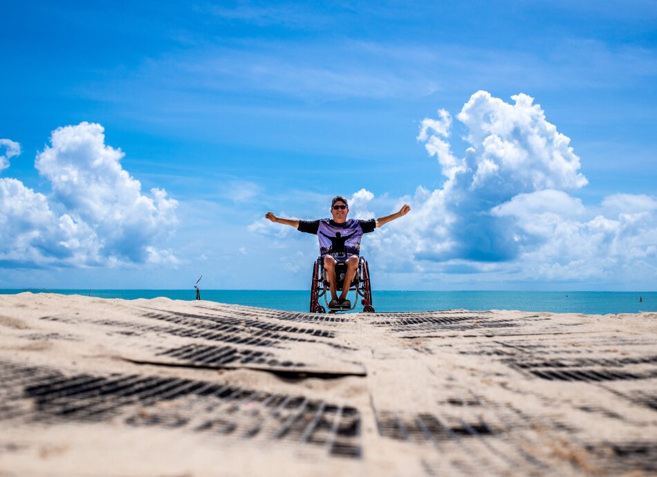 Triumphant man in wheelchair on beach with blue sky