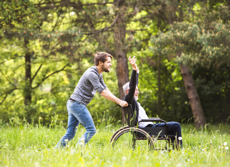 Young man pushing older man in wheelchair through grass