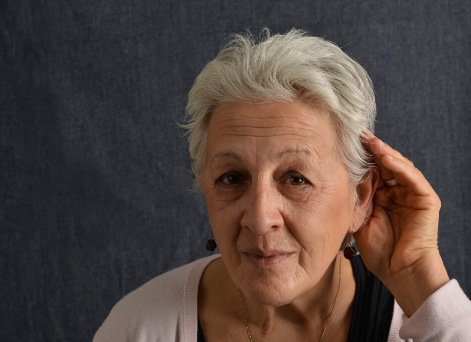 Older woman cupping her left ear with hearing loss
