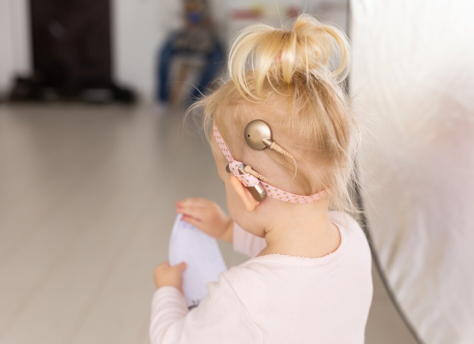 Cochlear implant on toddler's head with pink hairband