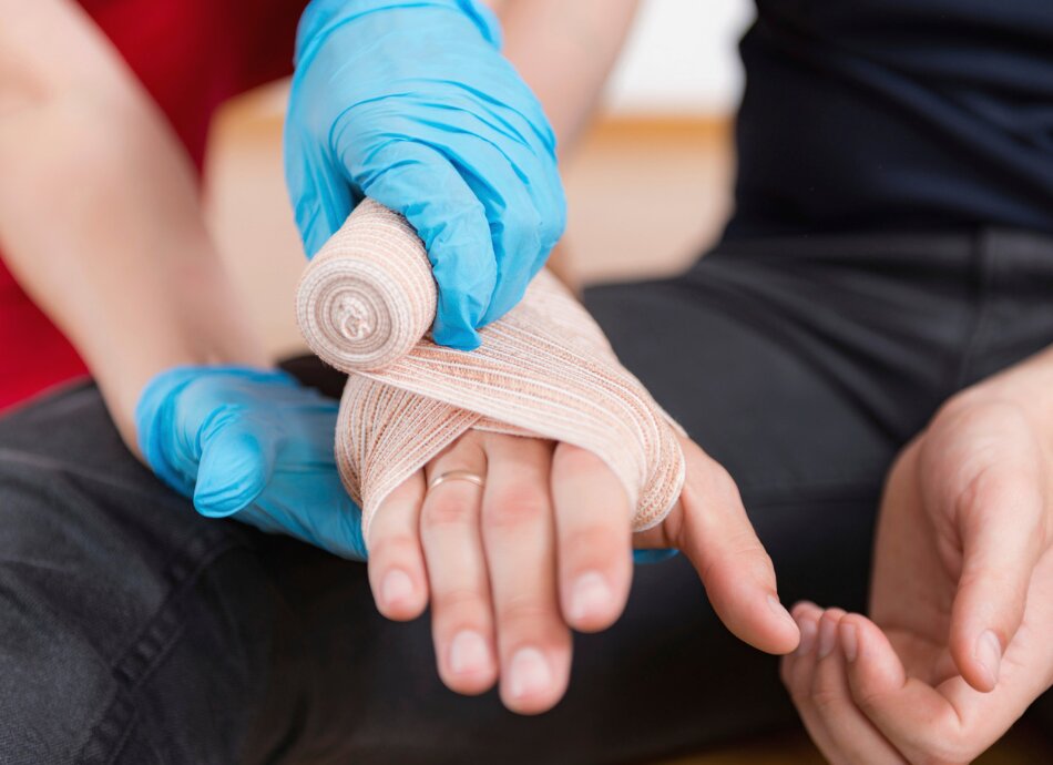 Hand being bandaged by someone wearing surgical gloves