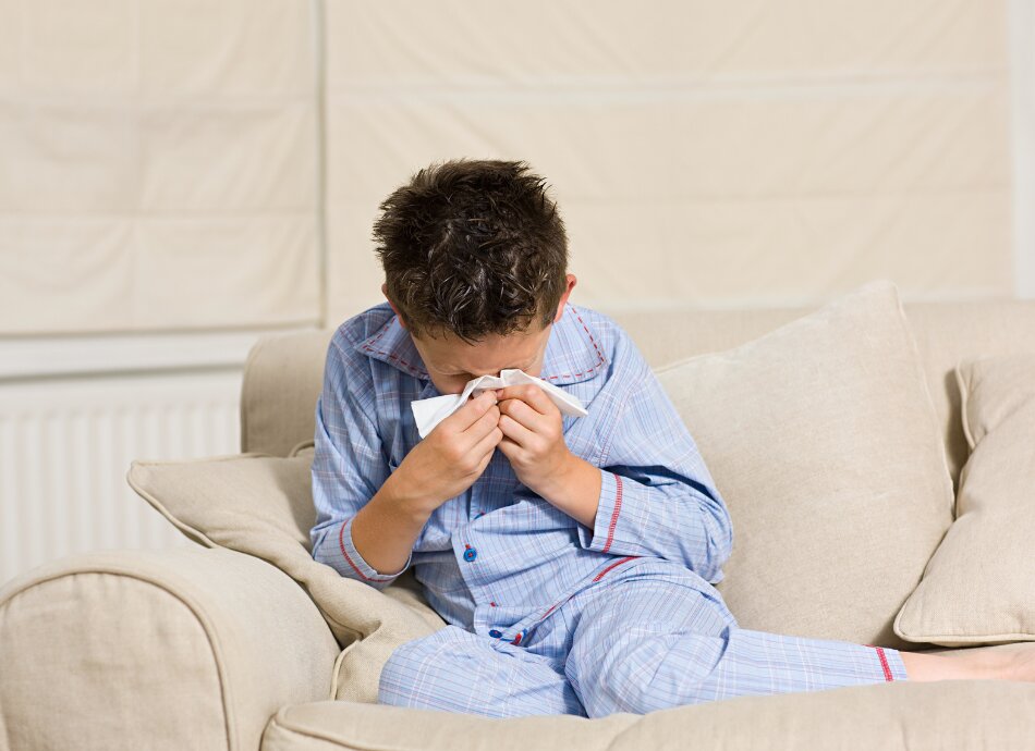 Boy in pyjamas on the couch sneezing into tissue
