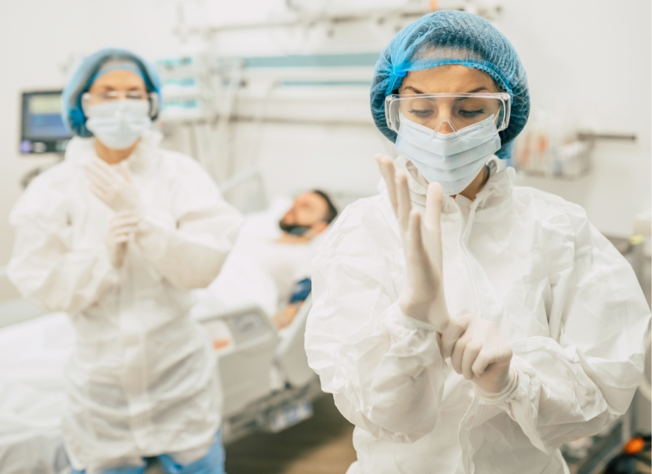 Hospital staff in PPE gear with man in background 