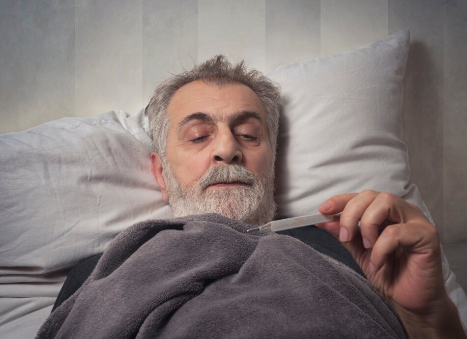 Older man in bed looking at thermometer