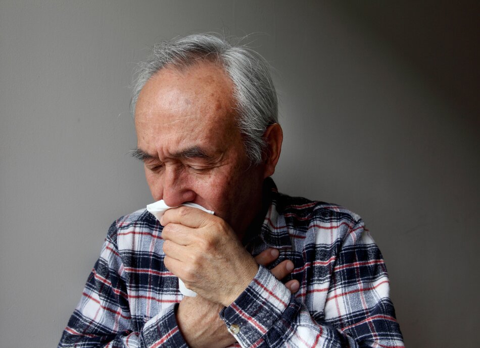 Older man holding handkerchief to mouth hand on chest 