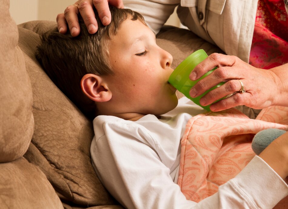 Unwell boy on couch sipping water 