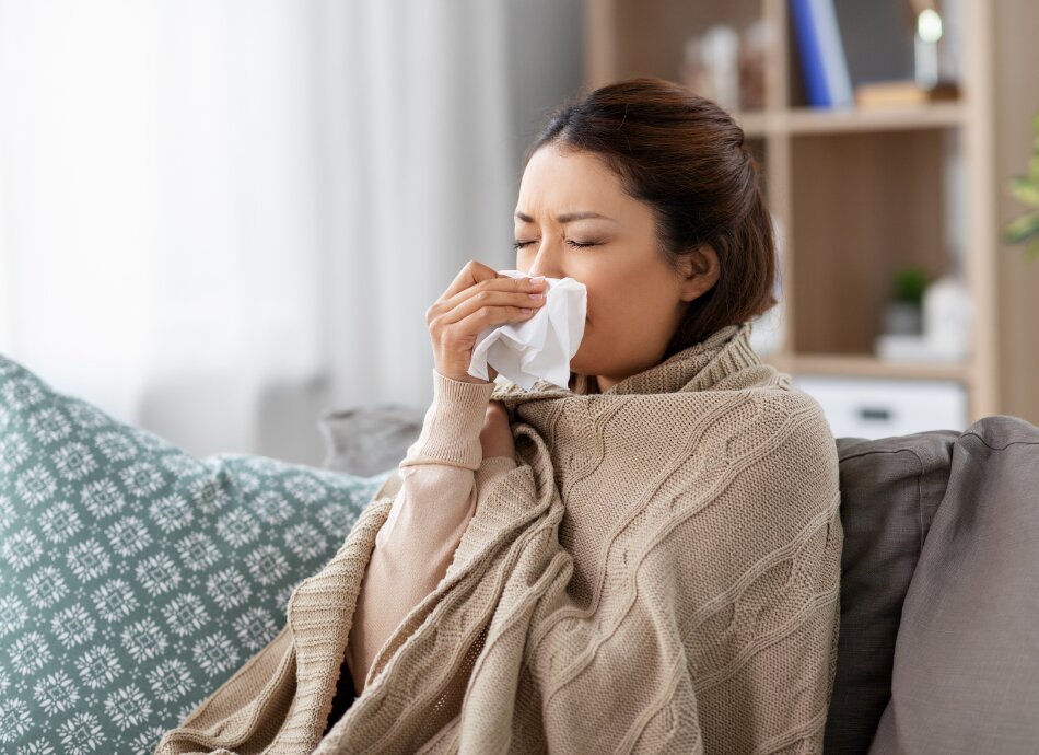 Woman blowing nose wrapped up on couch