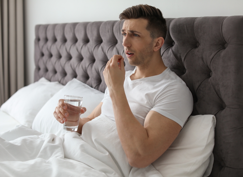 Man sitting up in bed taking pill with glass of water 