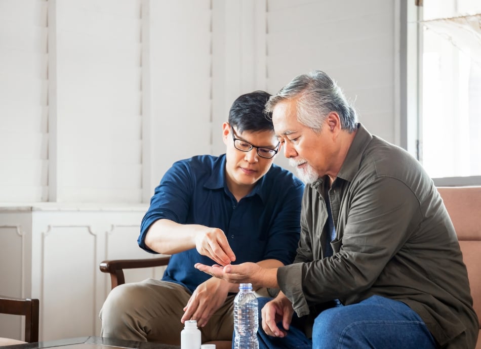 Son helping father take medicine with water 