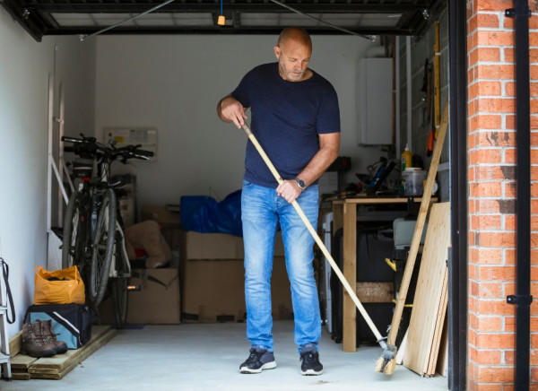 Man sweeping out his garage holding a broom