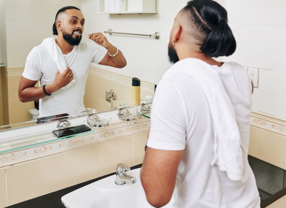 Man brushing teeth with reflection in mirror canva 950x690