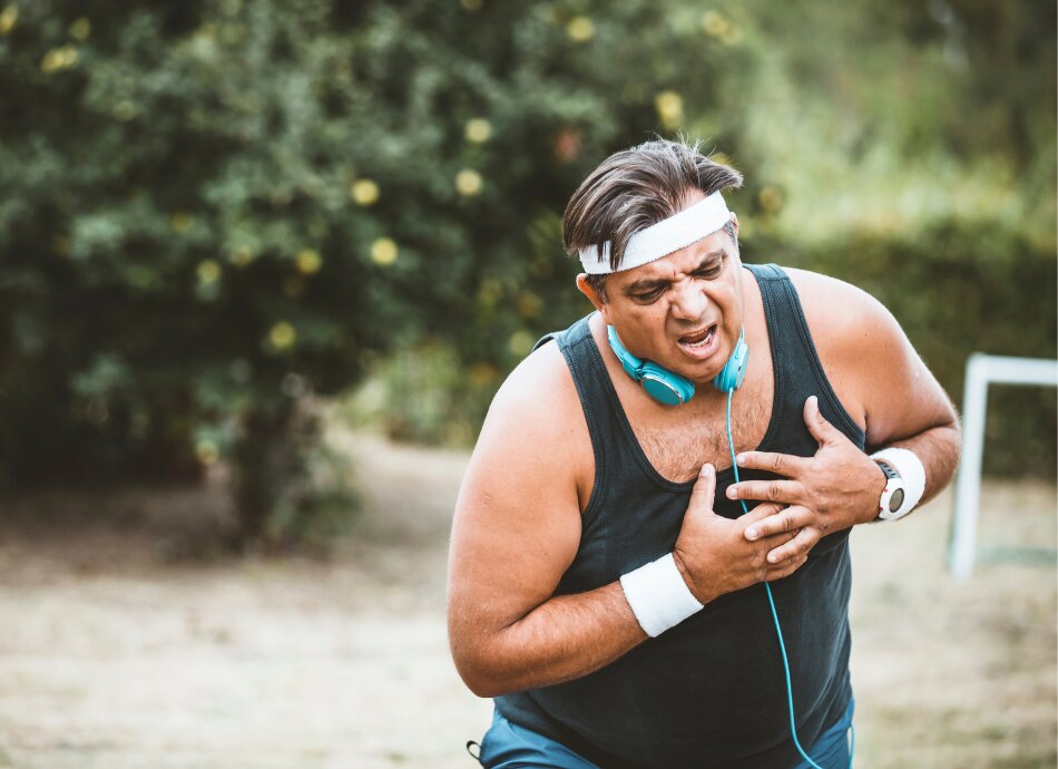 Sweaty man clutches chest in pain while outside running