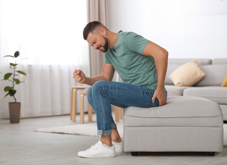 Man sitting on couch touches buttock in pain