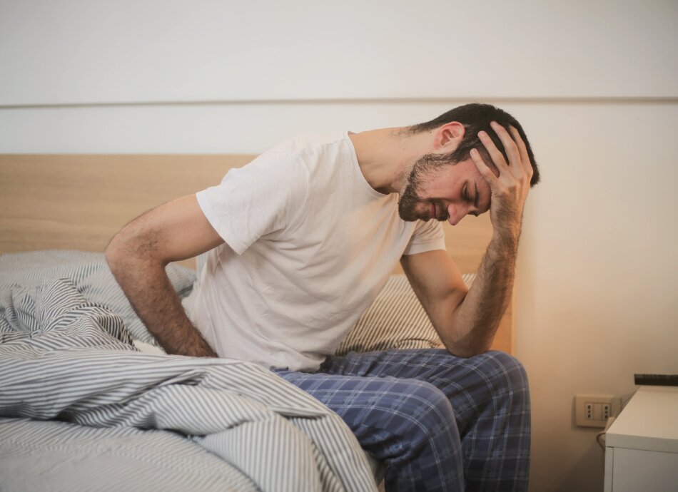 Man sits on side of bed holding his head in pain