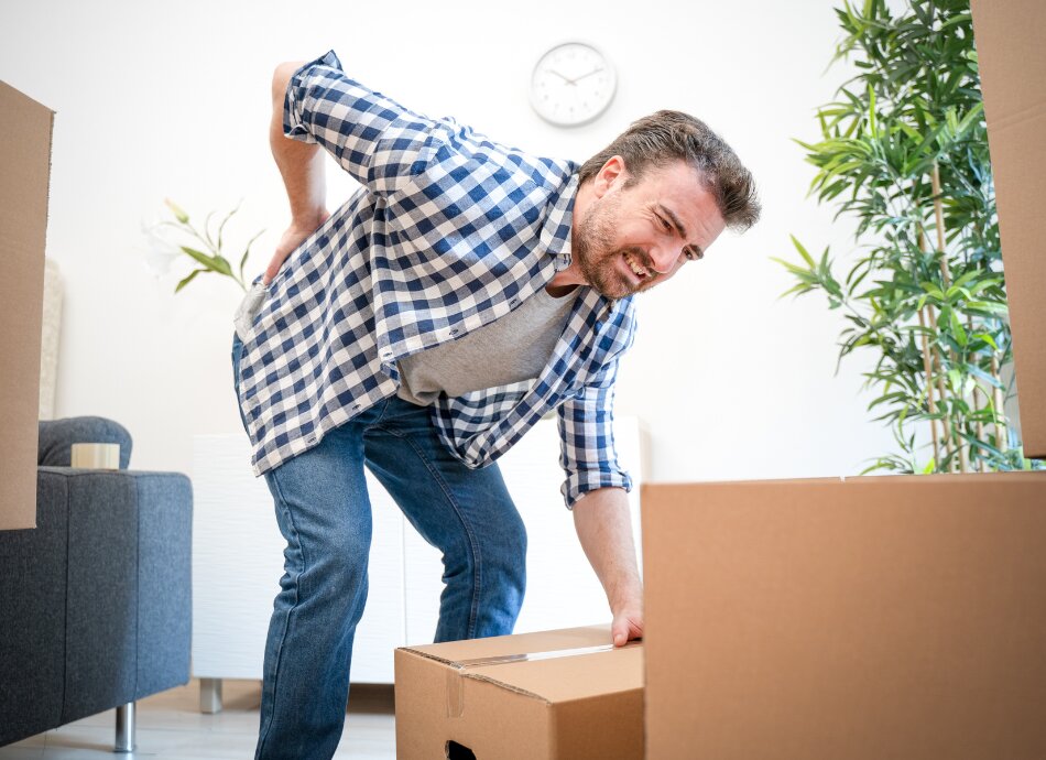 Man clutches sore back in pain while packing boxes
