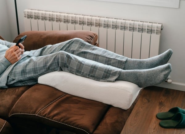 Person sitting down with legs elevated on pillow