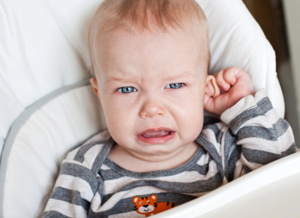 Small boy in highchair cries and pulls at his ear