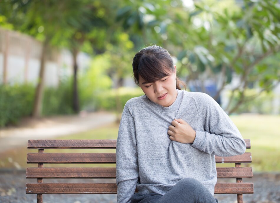 Young woman on park bench with reflux or indigestion holds chest