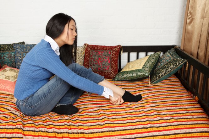 Woman sitting on bed putting socks on