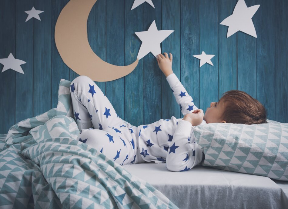 Young boy wearing starry pyjamas in bed with stars & moon on his wall