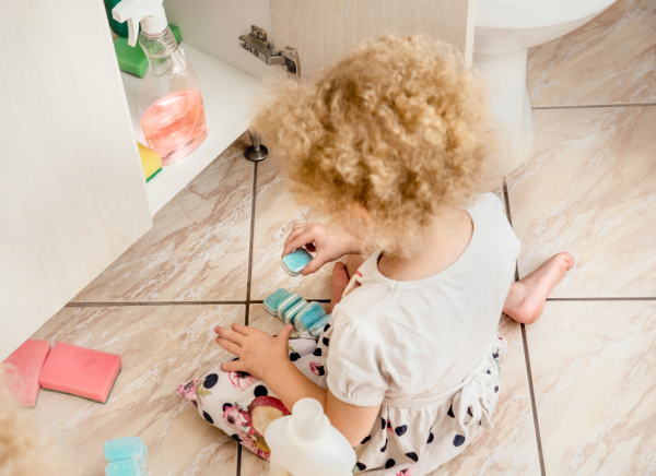 Child on floor by open cabinet playing with dishwasher tablets