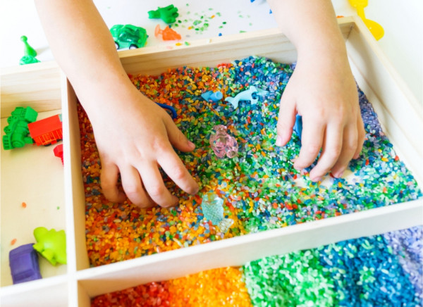 Child's hands feeling coloured rice in a sensory box