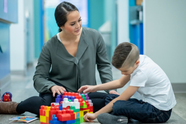 Occupational therapist helping boy play with coloured bricks