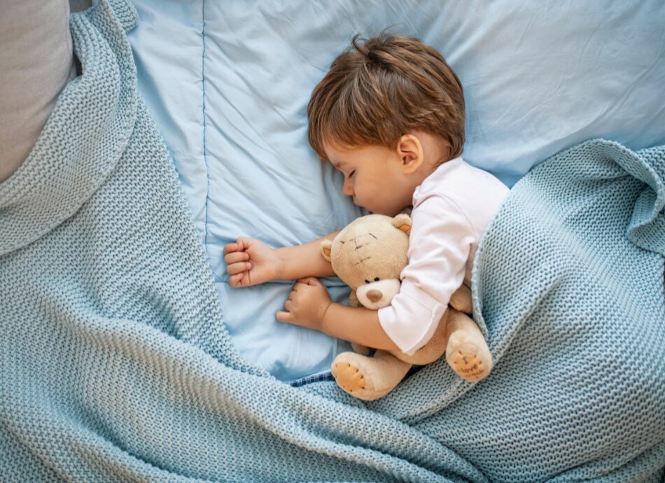 Young boy asleep in bed with teddybear