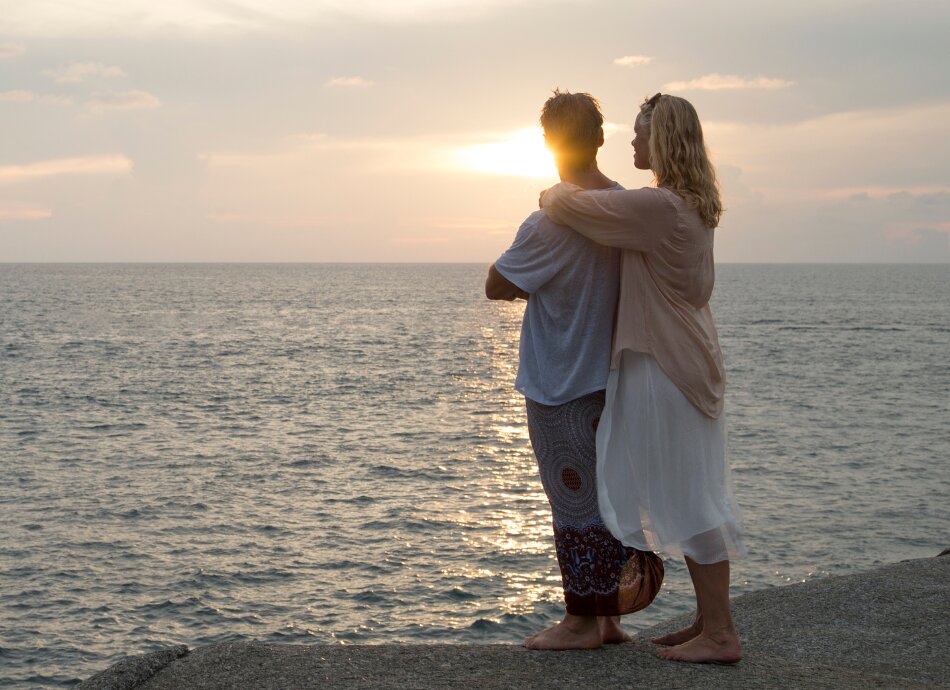 Young couple embracing looking out to sea at sunset
