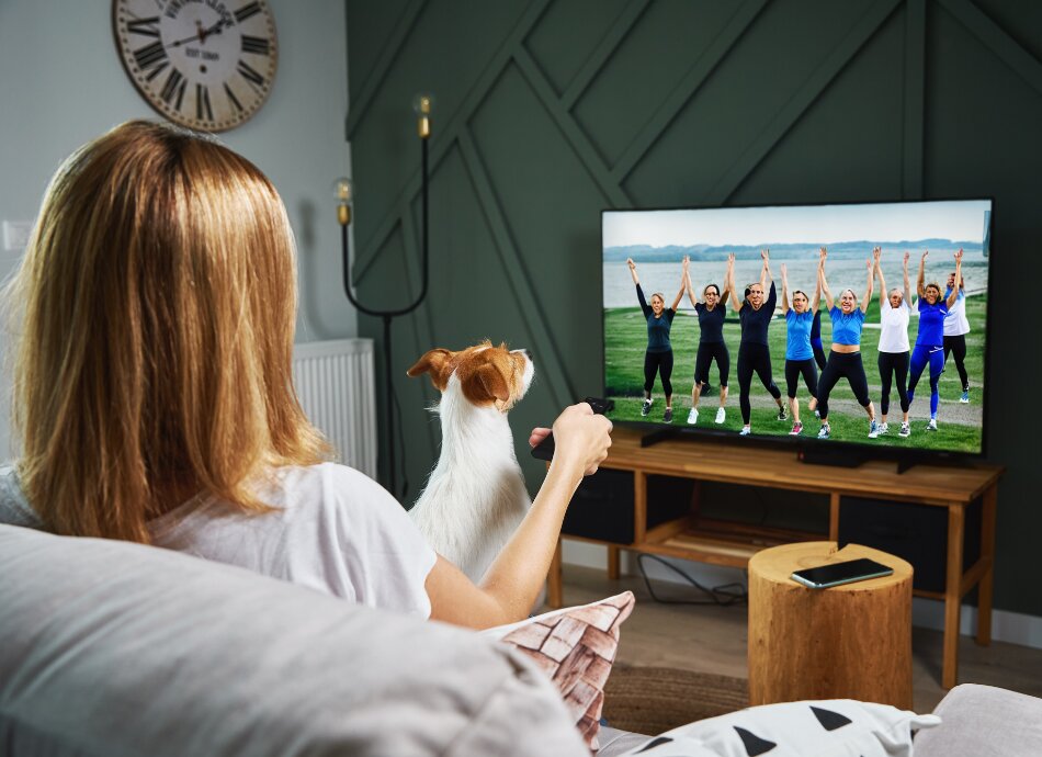 Woman and dog sitting on couch watching women exercising on tv
