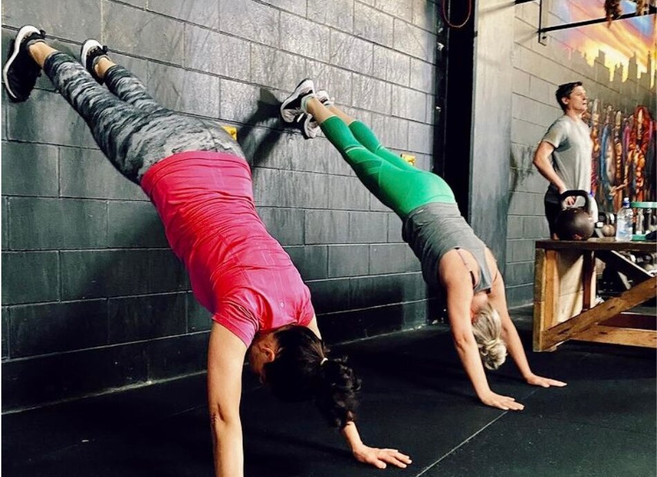2 women doing wall handstands in the gym