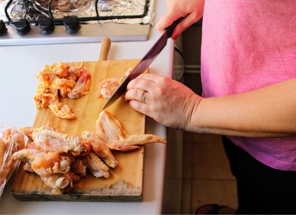 Cook chopping raw chicken meat on wooden board