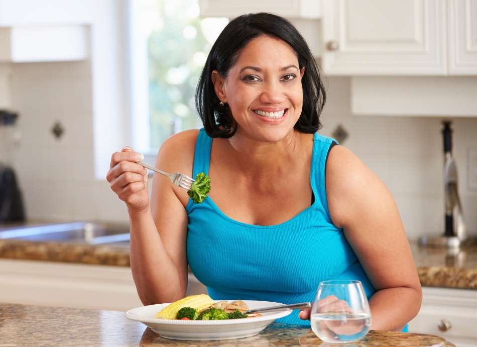 Smiling woman eating chicken and vegetables at home 
