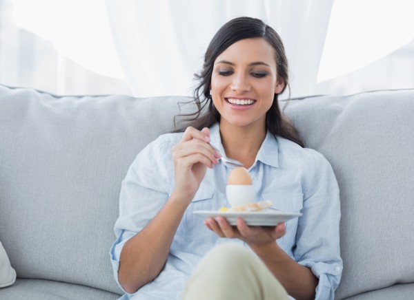 Woman sitting on couch eating a boiled egg