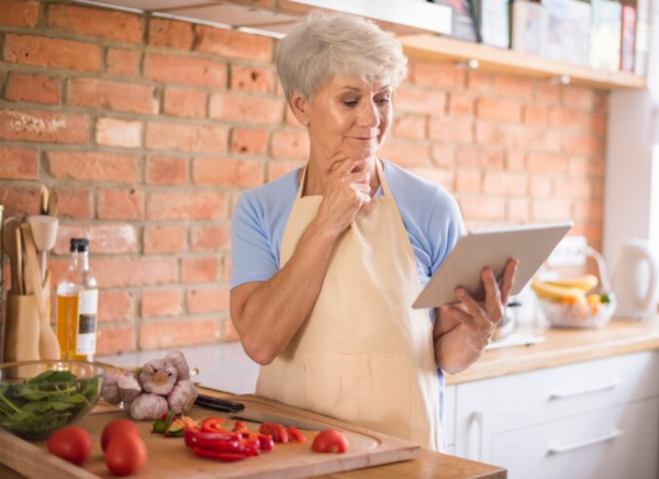 Woman cooking with fresh ingredients and looking at recipe on tablet