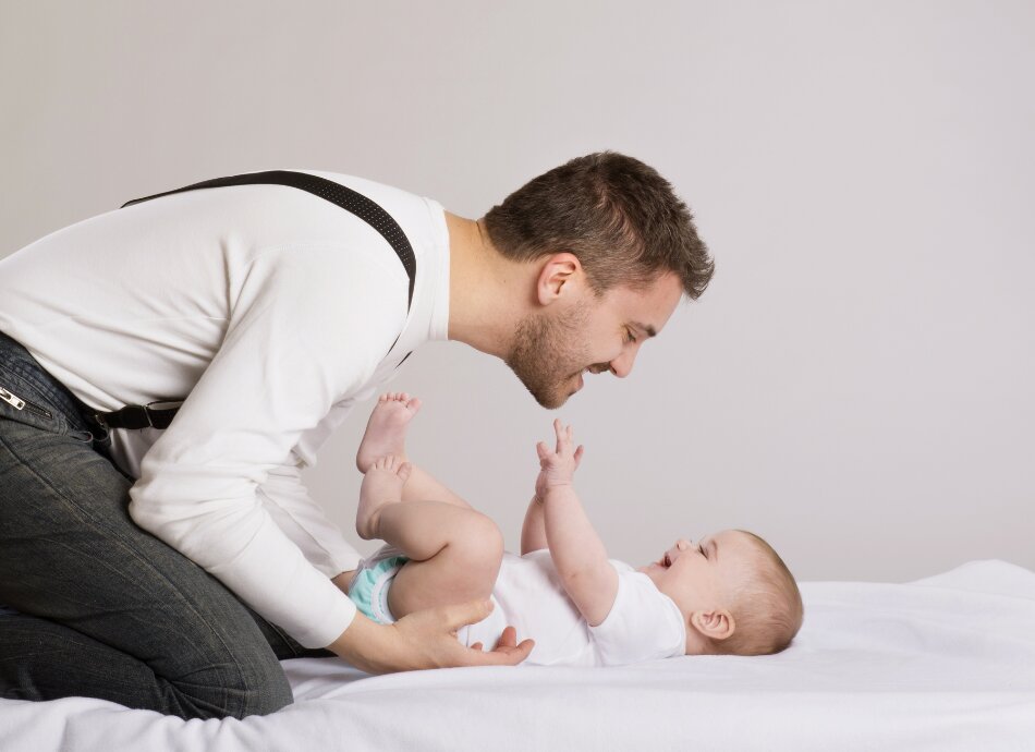 Father chats and smiles with baby on bed