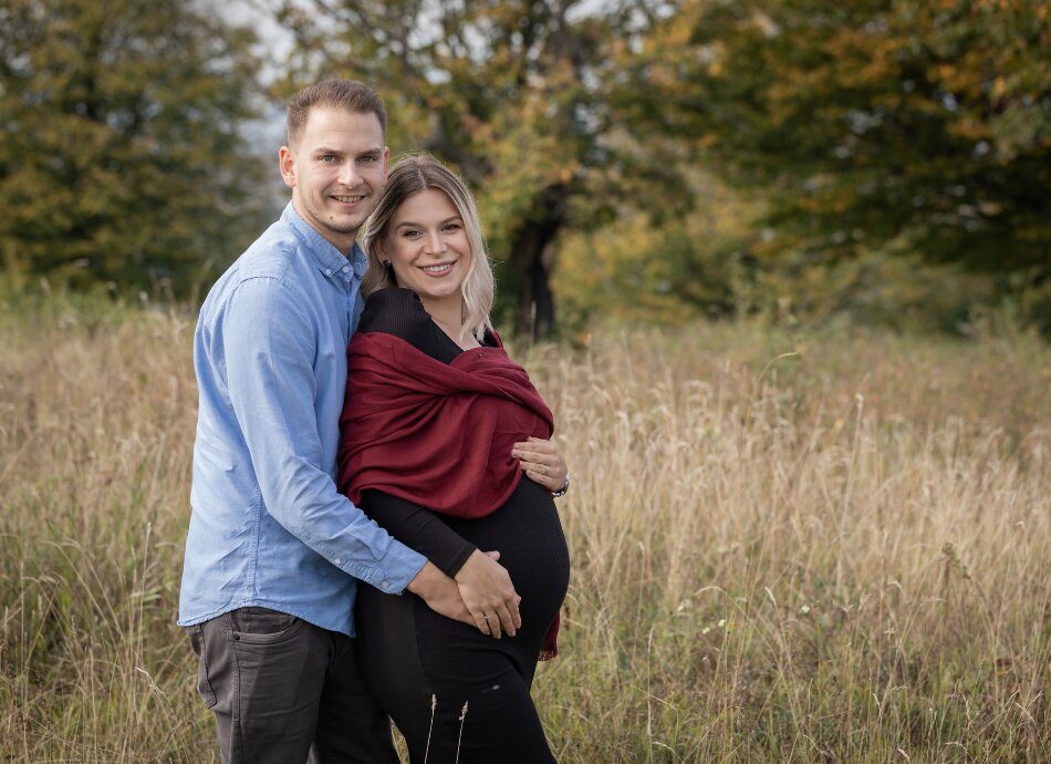 Pregnant couple in field as he holds her hand