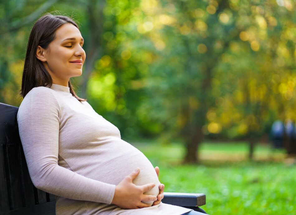 Pregnant woman sits on park bench in the sun