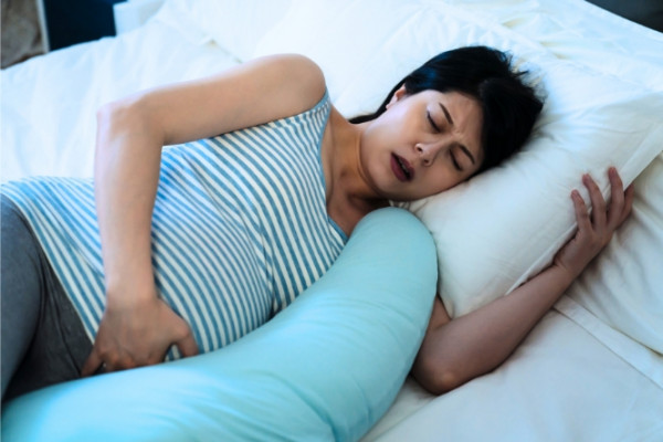 Woman with early labour pains lying in bed holding stomach