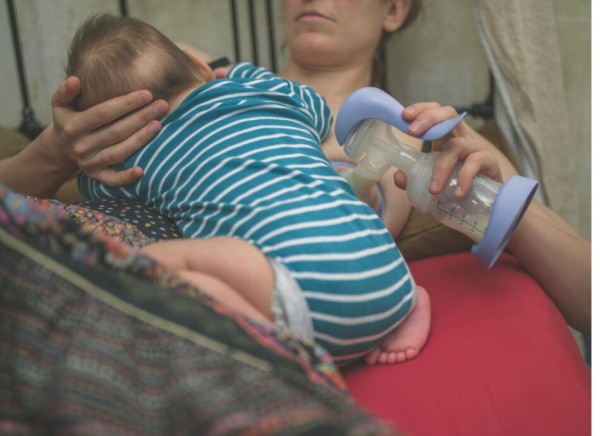 Persson breastfeeding and expressing milk with a hand pump at the same time