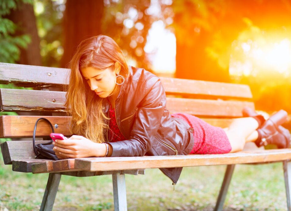 Girl lying on park bench looking at phone