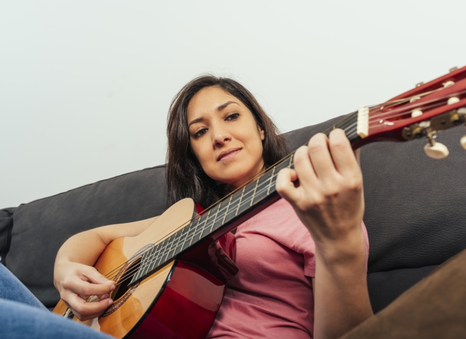 Young woman sitting on couch playing guitar 