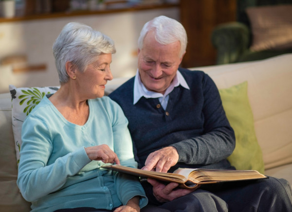 Older couple sitting on couch and looking through photograph album