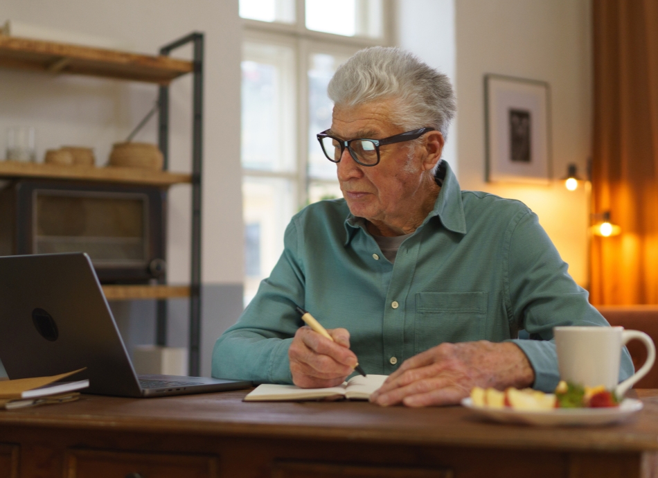 Older man sitting at computer taking notes 