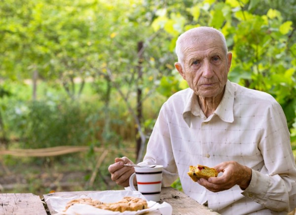 Thin older man sitting outside eating