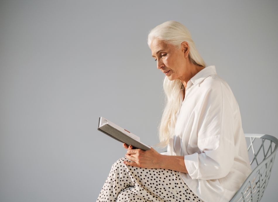 Older woman sitting cross legged on a chair reading a book 